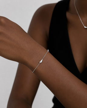 Kvinna som bär ett silverarmband med tunn kedja och droppe. 