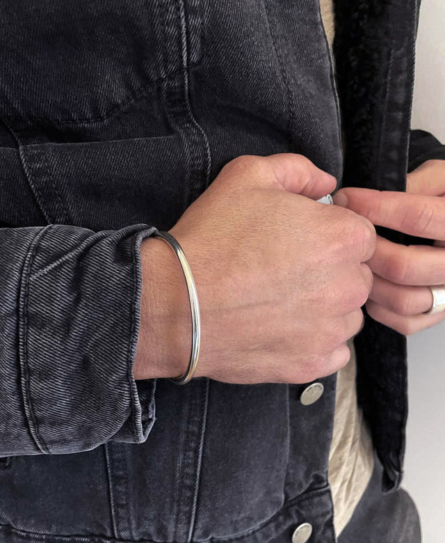 Kille i svart jeansjacka som bär ett stelt silverarmband. 