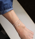 Tjej som bär tre smala silverarmband. En box / venezia kedja, en med kulor och ett armband med silverdroppe. 