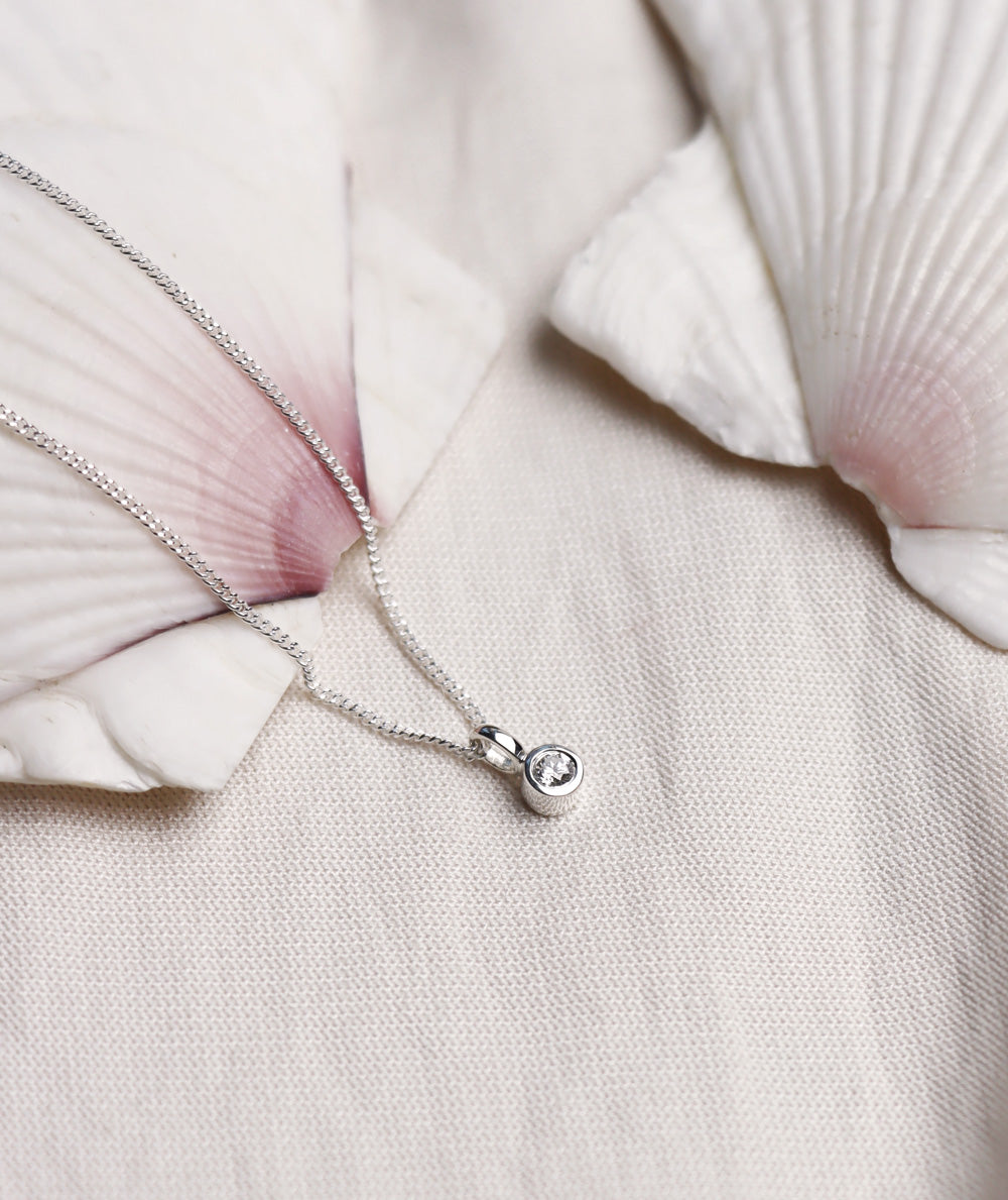 Närbild på halsband med briljantslipad diamant från Mila Silver placerad på en stor snäcka. 
