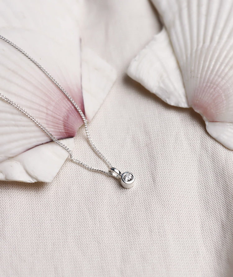 Närbild på halsband med briljantslipad diamant från Mila Silver placerad på en stor snäcka. 