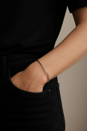 kvinna som bär ett stelt silverarmband med blank slät yta. hon har svarta jeans och svart topp. 