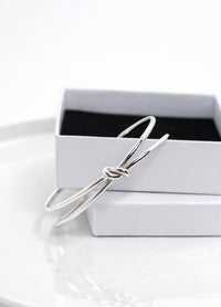 Stelt silverarmband med knut placerat på en vit smyckesask. 