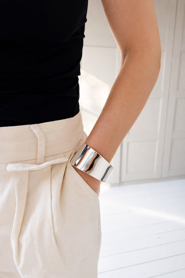 Kvinna som bär ett brett cuff armband i blankt silver. 