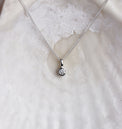Närbild på ett diamant hängsmycke i kedja med en gnistrande diamant i silverfattning utformad som ett rör. 