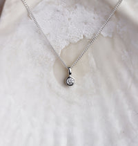 Närbild på ett diamant hängsmycke i kedja med en gnistrande diamant i silverfattning utformad som ett rör. 
