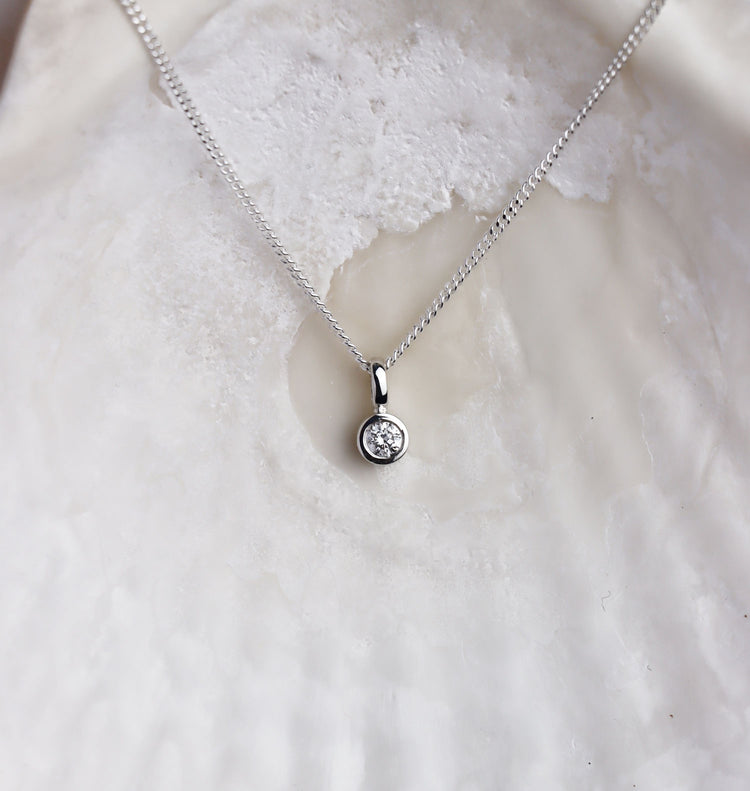 Närbild på ett diamant hängsmycke i kedja med en gnistrande diamant i silverfattning utformad som ett rör. 