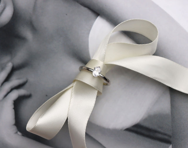 En diamantring med oval stor diamant placerad på en sidenrosett. 