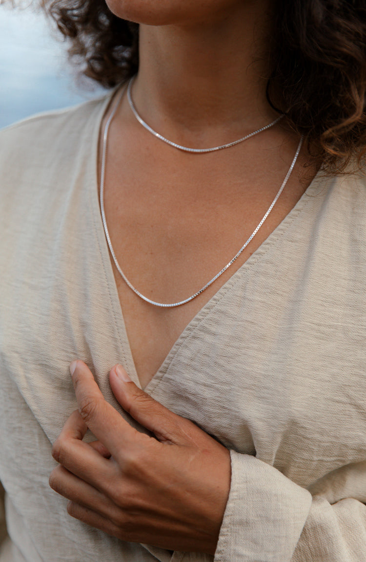 Kvinna som bär tunna silverkedjor som halsband i olika längder. Kedjehalsband, modell: Box chain / Venezia kedjor
