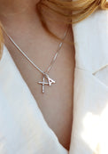 Tjej som bär ett silverhalsband med silverkors och bokstavsberlock. 