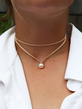 Tjej som bär ett halsband med virat läderband runt halsen med en vit pärlberlock och diamant. 