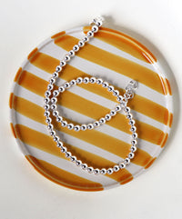 Silverhalsband med kulor placerat på ett gul- och vit randigt fat. 