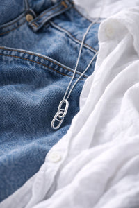Silverhalsband med länkar i kedja som ligger på ett par blå jeans. 