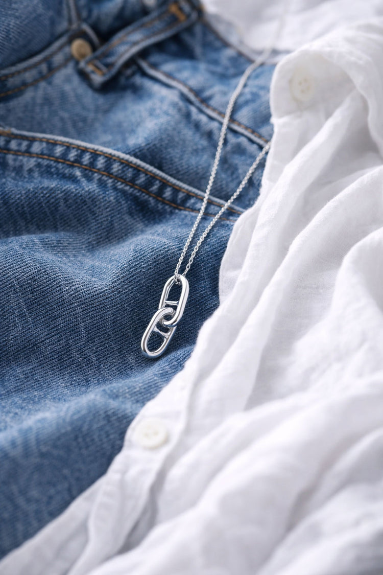 Silverhalsband med länkar i kedja som ligger på ett par blå jeans. 