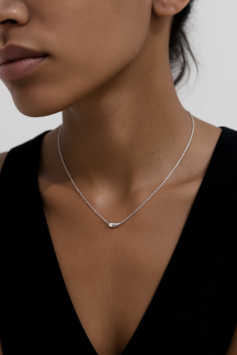kvinna som bär ett tunt silverhalsband med en liten silver droppe. 