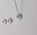Silverhalsband med ett hängsmycke utformat som ett hjärta med organiska former, sett från sidan. 
