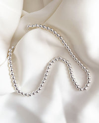 Halsband med silverkulor placera på ett vitt böjande tyg. 