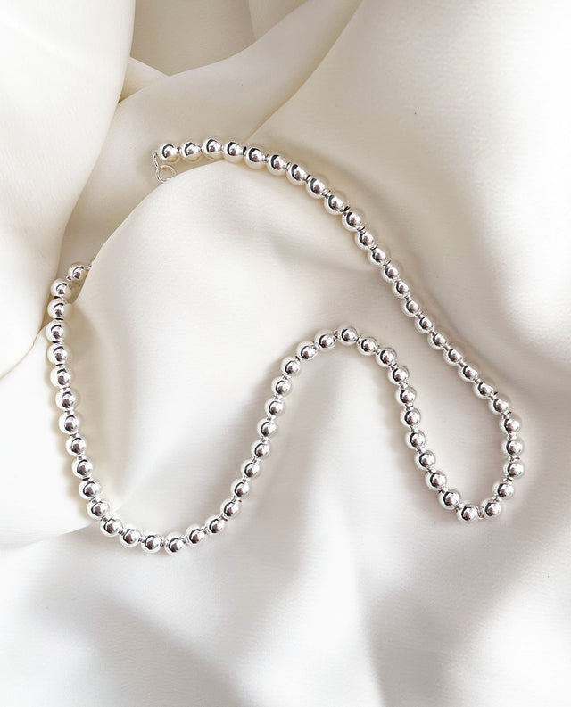 Halsband med silverkulor placera på ett vitt böjande tyg. 