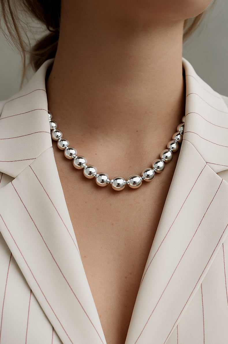 tjej som bär ett stort silverhalsband med stora silverkulor till vit kavaj . 