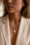 Kvinna som bär ett halsband med silverkedja och stor pärla med barock-form. hon bär vit kavaj med djup urringning. 