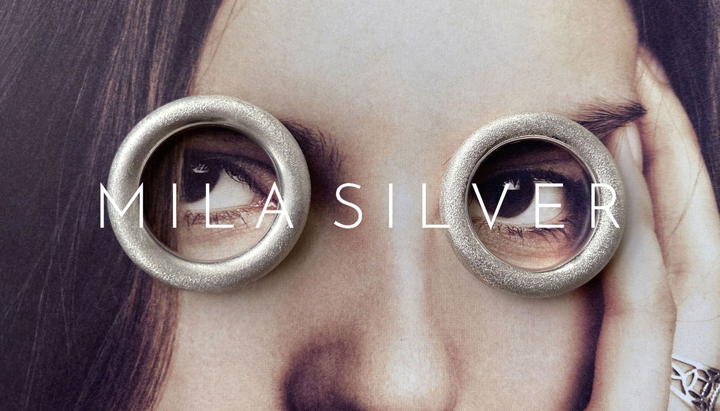 Två silverringar placerade runt ett fotografi på två ögon. Mila Silver logga placerad rak över bilden över ögonen. 