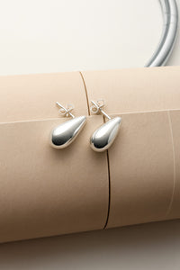 silverörhängen med droppar placerade på en ihoprullat beige tidning