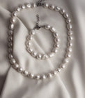 halsband och armband med stora ojämna vita pärlor placerade på ett vitt sidentyg. 