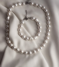 halsband och armband med stora ojämna vita pärlor placerade på ett vitt sidentyg. 