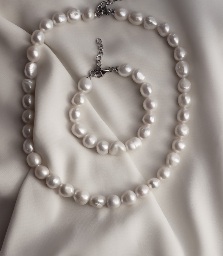 halsband och armband med stora ojämna vita pärlor placerade på ett vitt sidentyg. 