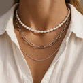 tjej som bär flera halsband i olika längder. Ett pärlhalsband, ett halsband med kedja och en tunn silverkedja. 
