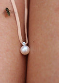 Berlock med pärla och diamant i läderband, placerad mellan två ben, ett litet bi kryper på benet. 