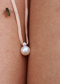 Berlock med pärla och diamant i läderband, placerad mellan två ben, ett litet bi kryper på benet. 