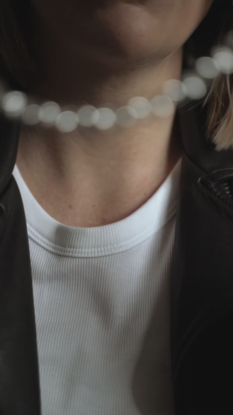 Kvinna som tar på sig ett halsband med silverkedja som har stora länkar.  