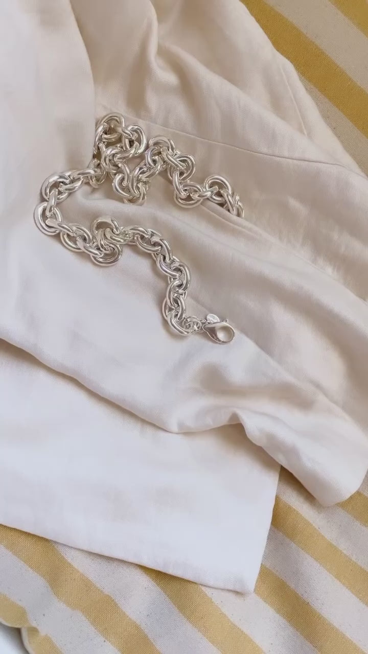 Kvinna som tar på sig ett halsband med stor chunky silverkedja. 