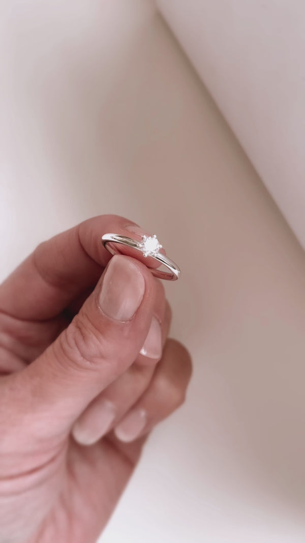 Film som visar en vigselring eller förlovningsring i silver med rund diamant som glänser.