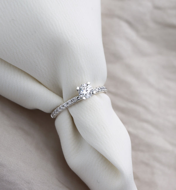 Diamantring med sidostenar och en stor diamant i mitten, placerad runt ett vitt tyg. 