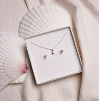 Ett set med matchande diamantsmycken placerade i en vis ask som ligger på två stora vita snäckor. 