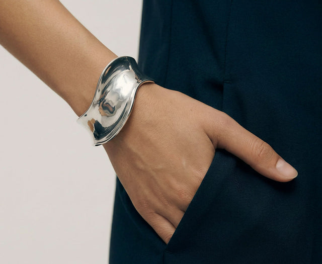 Tjej som bär ett brett stelt silverarmband med böjd form. 