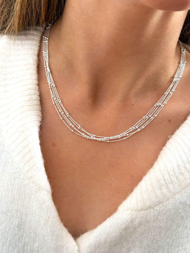 Tjej som bär ett kort halsband i silver med tunna kedjor och små silverkulor. 