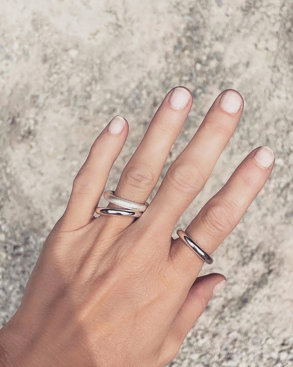 Tjej som bär tjocka silverringar på olika fingrar. Ringarna är släta, blanka och en ring har matt yta. 