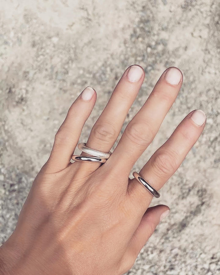 Tjej som bär tjocka silverringar på olika fingrar. Ringarna är släta, blanka och en ring har matt yta. 