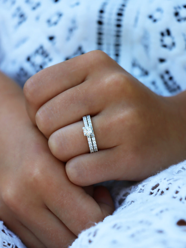 Tjej som bär ett set med vigsel och förlovningsringar med diamanter. Ringarna är täckta med små diamanter runt om ringarna. Den ena ringen har en stor diamant i mitten. 