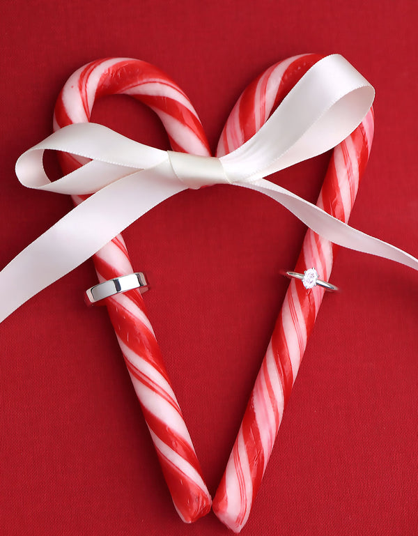 En julig bild med förlovningsringar till dam och herr placerade på ett rött hjärta av polkagrisar. Ring par med silverring till herr och diamantring till dam. 