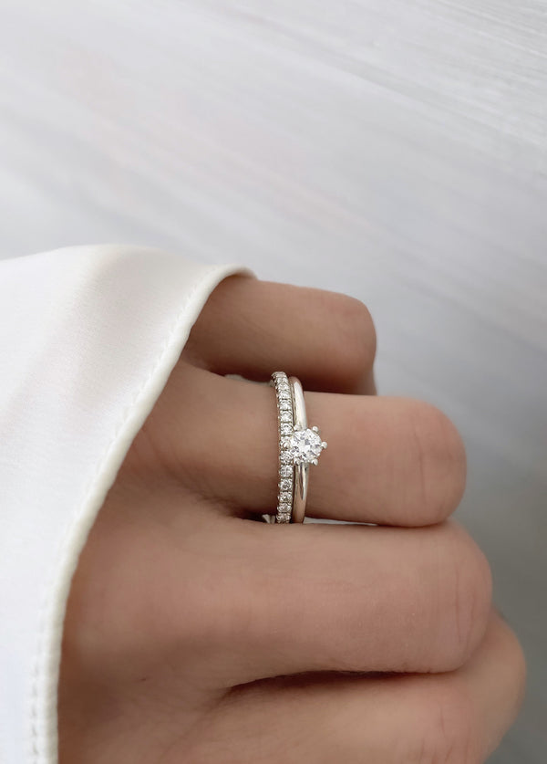 En tjej som bär ett set med vigselring och förlovningsring på vänster ringfinger. Ringarna har vita gnistrande diamanter. Alliansring + solitärring. 