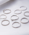 Många silverringar placerade på ett bord. Ringen i mitten har en diamant i bezel fattning. 