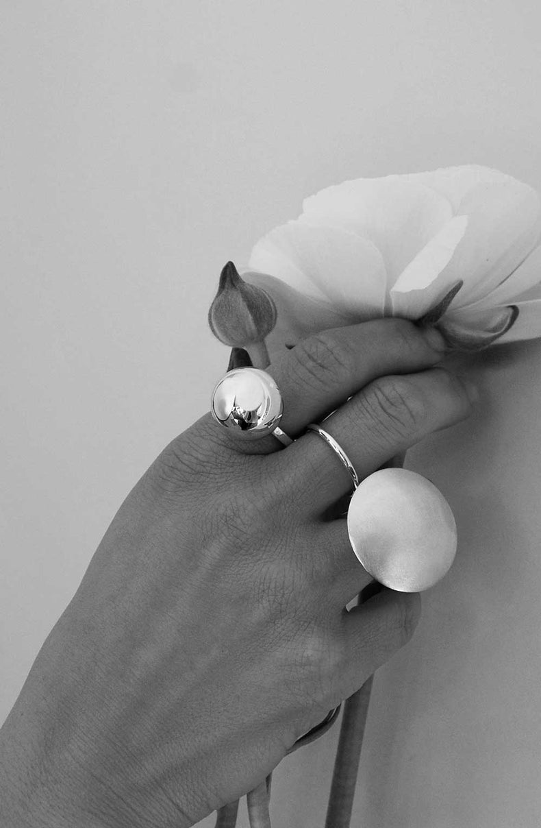 Kvinna som bär en stor silverring med en stor silverkula i kombination med andra stora silverringar i äkta silver. Hon håller i en vit tulpan. 